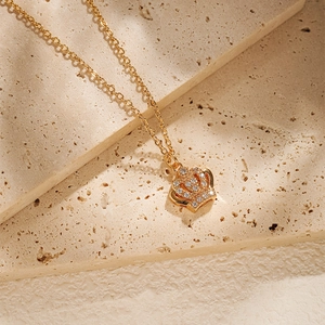 Détail d'un pendentif couronne doré orné de zircons posé sur une surface en pierre