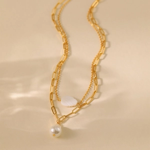 Close-up of double-layered gold necklace with white leaf shell and pearl pendant detail