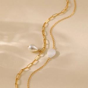 Macro detail of 18K gold-plated layered necklace with baroque pearl and leaf pendant