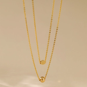 Polished 18K gold plated double layer necklace with bead and disc pendants in soft light