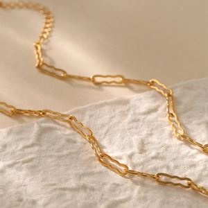 Detalle de collar chapado en oro con eslabones rectangulares sobre fondo de papel blanco