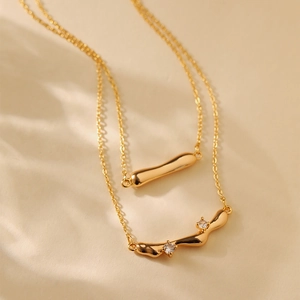 Detail of double-layer gold necklace featuring wavy pendant with zircon stone accents