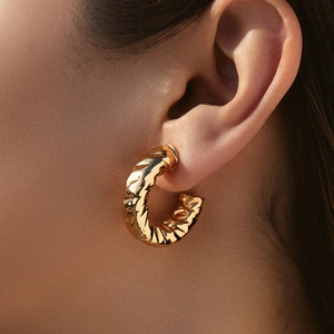 Irregular C-shaped gold hoop earrings with rippled texture on a model's ear