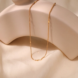 Detalle de collar dorado minimalista con eslabones geométricos sobre una tela suave