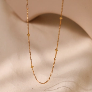 Detalle de collar de clavícula dorado con colgantes de rombo pulidos y eslabones mixtos