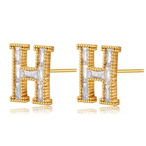Gros plan de boucles d'oreilles en forme de H dorées avec trois zircons rectangulaires