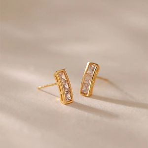Gros plan sur des boucles d'oreilles dorées avec trois zircons carrés verticaux