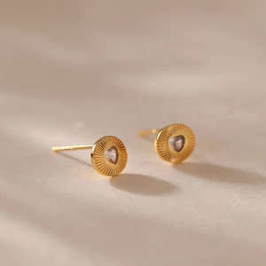 Détail macro d'une boucle d'oreille dorée avec zircon en cœur et texture rayonnante