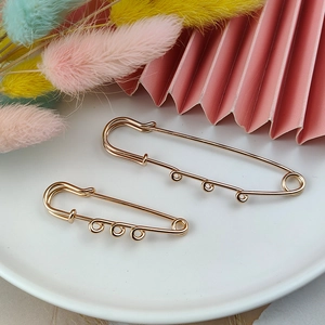 Golden safety pins with three loops for DIY jewelry making on a white plate