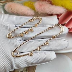 Polished gold safety pin brooches in two sizes held by a silver gloved hand with flowers