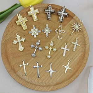 Assorted gold and silver cross pendants with pearls and rhinestones on a wooden tray