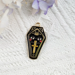 Détail d'un pendentif cercueil en émail noir avec croix dorée sur tricot blanc