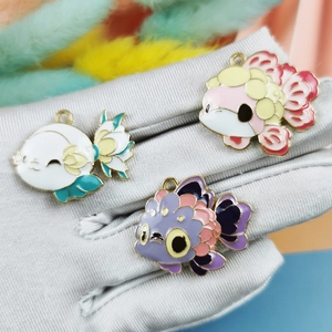 Three colorful enamel fish charms in alloy for DIY jewelry making on a grey display glove