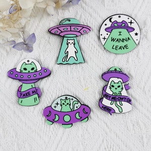 Pendentifs en émail chat et OVNI vert menthe et violet sur un fond blanc avec texture