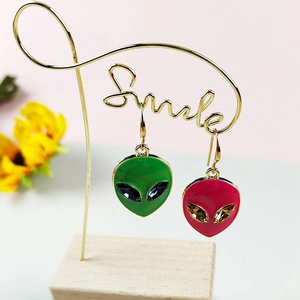 Enamel alien head charm earrings with crystal eyes on a decorative smile display stand