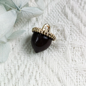 Macro detail of acorn pendant with dark brown enamel and golden textured metal cap