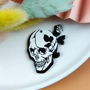 Macro shot of skull and rose acrylic pendant on white plate with dried flower decor
