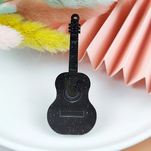 Detail of guitar-shaped acrylic charm with white glitter specks on black surface