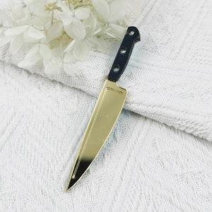 Close-up of a miniature Halloween chef knife charm with a golden mirror finish