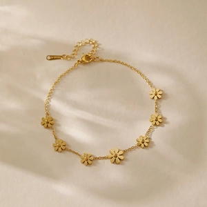 Detailed shot of golden chain bracelet with delicate daisy charms on textured fabric