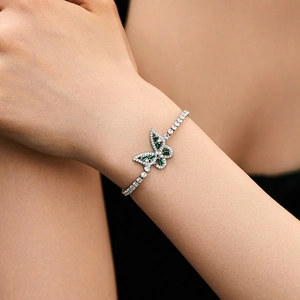 Close-up of minimalist butterfly bracelet with green emerald-cut stones on model wrist