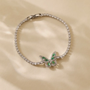 Detailed macro view of silver bangle with zircon chain and green emerald butterfly