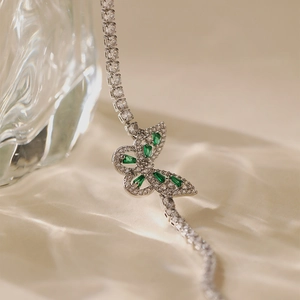 Macro view of butterfly charm with green stones on a sparkling silver tennis bracelet