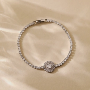 Macro view of silver tennis bracelet featuring a halo-set round crystal pendant