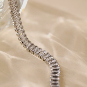 Detail of a silver tennis bracelet with baguette-cut zircons on champagne silk fabric