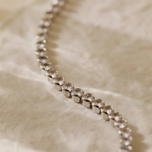 Macro shot of silver tennis bracelet with cubic zirconia set on white textured paper