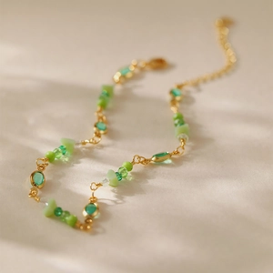Detalle de una tobillera dorada con cuentas de cristal verde y piedras naturales