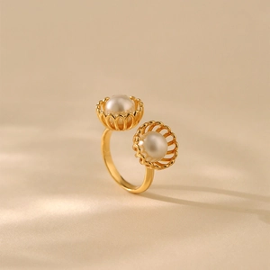 Eleganter goldener Ring mit zwei weißen Perlen in floraler Fassung auf beigem Hintergrund