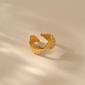 Eleganter vergoldeter offener Ring mit Federblatt-Textur auf warmem beigem Hintergrund