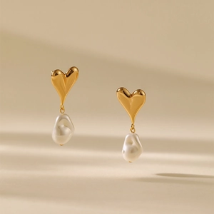 Elegant gold heart earrings with natural baroque pearl drops on a warm beige background