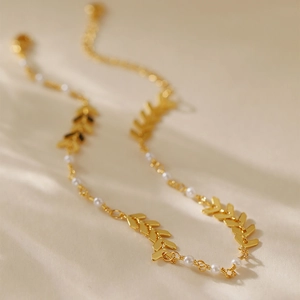 Detalle de la tobillera dorada de espina con perlas blancas sobre fondo crema suave