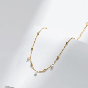 Detalle de tobillera bohemia dorada con perlas blancas delicadas y pequeñas bolas de oro