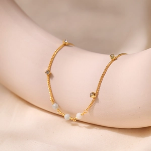 Detalle de tobillera bohemia dorada con piedras de cristal y cuentas claras