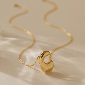 Detailed close-up of a high-polish gold plated C-shaped pendant on a fine link chain