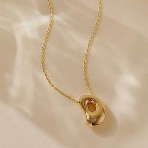 Detailed view of an organic bean-shaped hollow gold pendant on a fine link chain necklace
