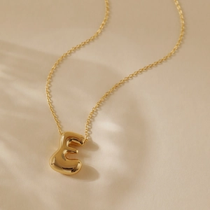 Close-up of gold 3D bubble letter E pendant on a delicate chain necklace