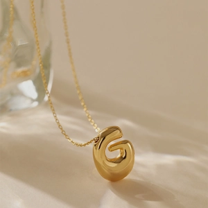 Detailed view of polished gold plated letter G pendant with artistic ripple light effects