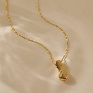 Close-up of gold plated organic alphabet pendant necklace on textured fabric with soft light