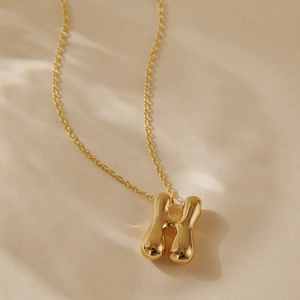 Macro detail of gold plated letter H pendant with glossy mirror finish on dainty chain