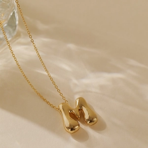 Macro detail of high-polish gold bubble letter M pendant on a fine link chain necklace