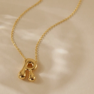 Macro detail of gold-plated liquid metal letter R pendant on a thin link chain