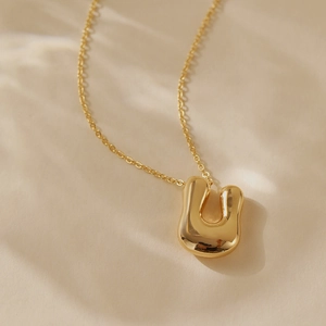 Macro detail of high-polish gold plated 26 letters necklace featuring bubble letter U pendant