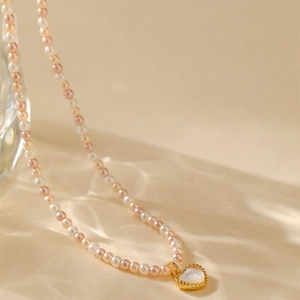 Roze en witte parelketting met een gouden hart hanger op een waterrimpel achtergrond