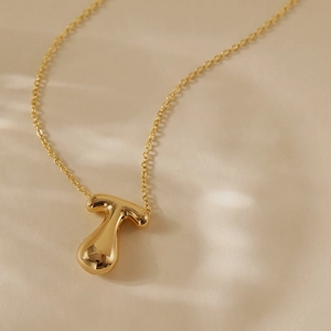 Macro shot of 18k gold plated letter T pendant with a polished mirror finish on a link chain