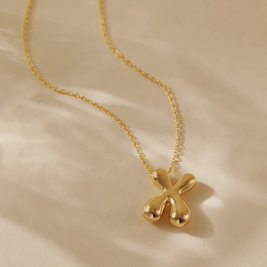 Detail of 18K gold-plated necklace featuring a fluid mirror-polished X-shaped pendant
