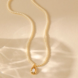 Franse retro parelketting met onregelmatige gouden hanger op een crème achtergrond